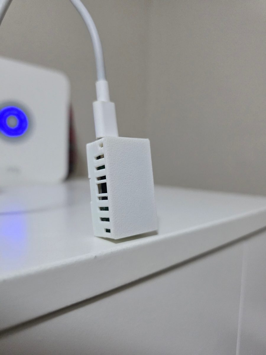 Sensore Apollo MSR-2 in piedi sul piano di un mobile bianco, con il cavo USB-C collegato in alto e le fessure del case ben visibili