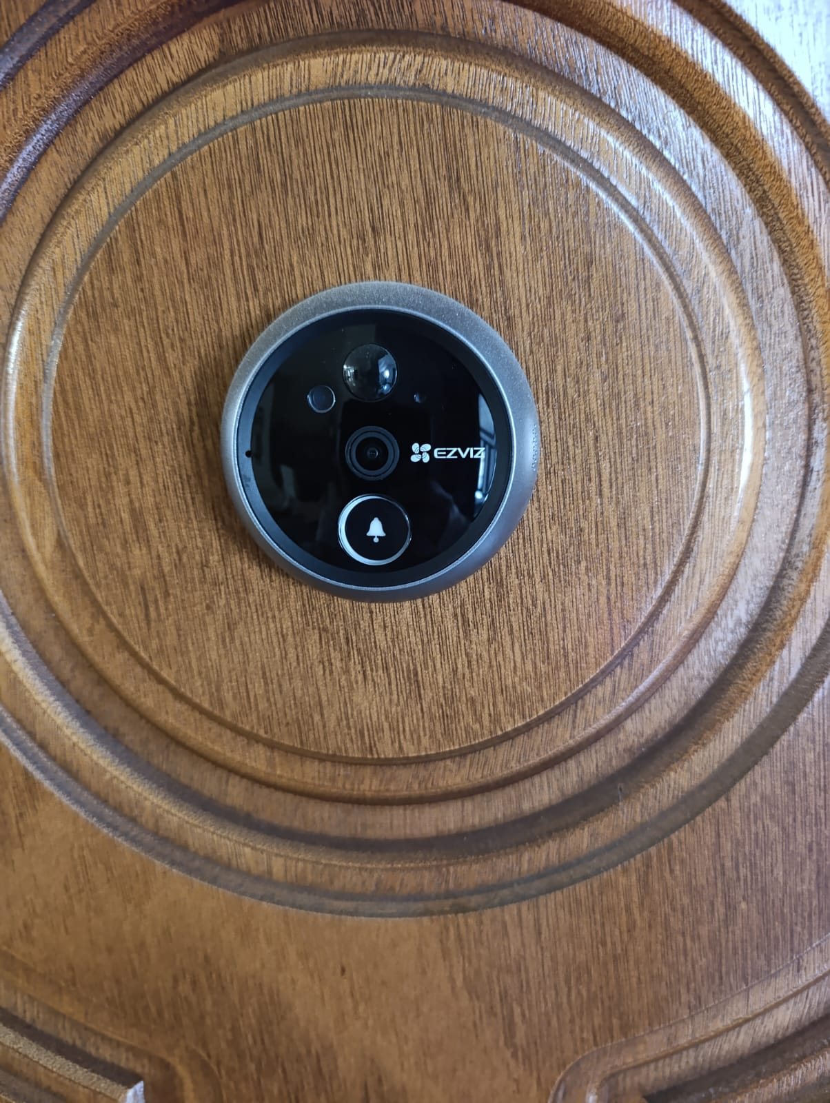 Telecamera esterna dell'EZVIZ CP4 sulla porta in legno, con obiettivo, sensore e pulsante del campanello