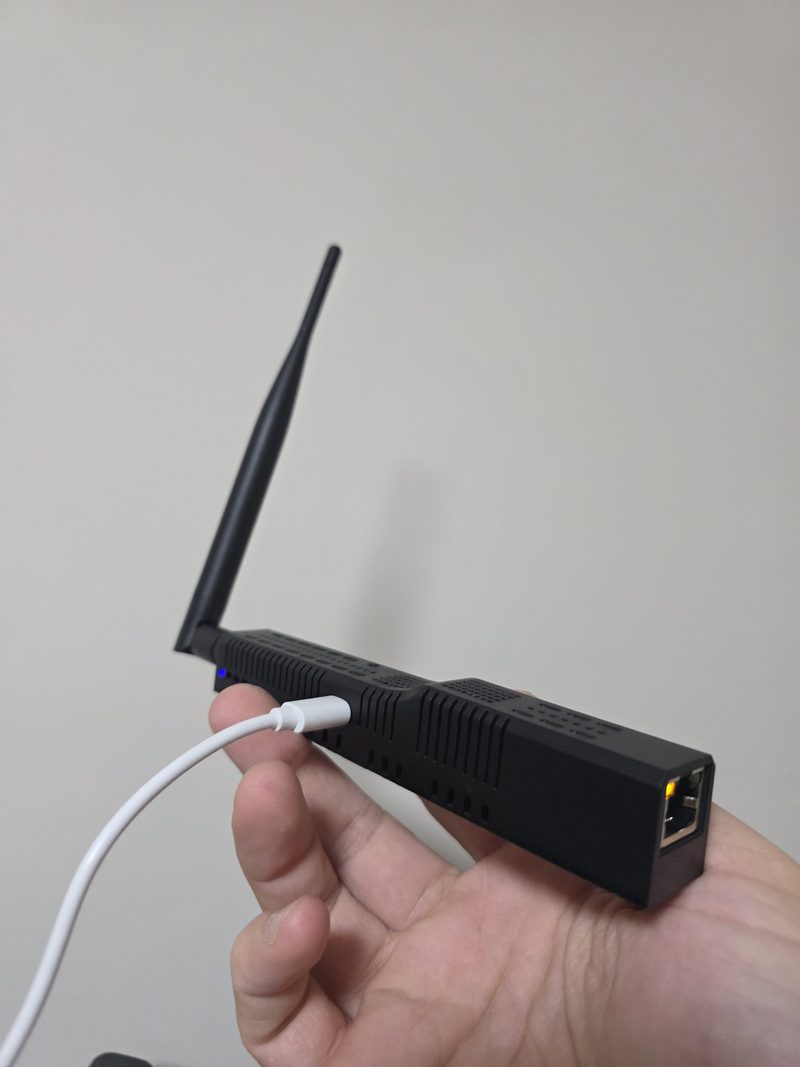 SMHUB Nano tenuto in mano, con l'antenna avvitata, il cavo USB-C bianco e la presa di rete in fondo